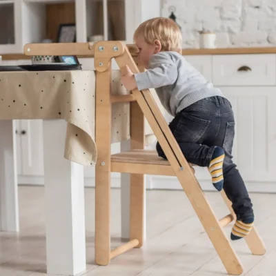 Peuter klimt enthousiast op houten Montessori leertoren in keukenomgeving